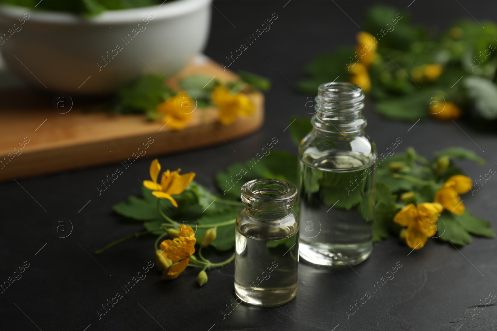 Photo of Bottles of natural celandine oil near flowers on black table
