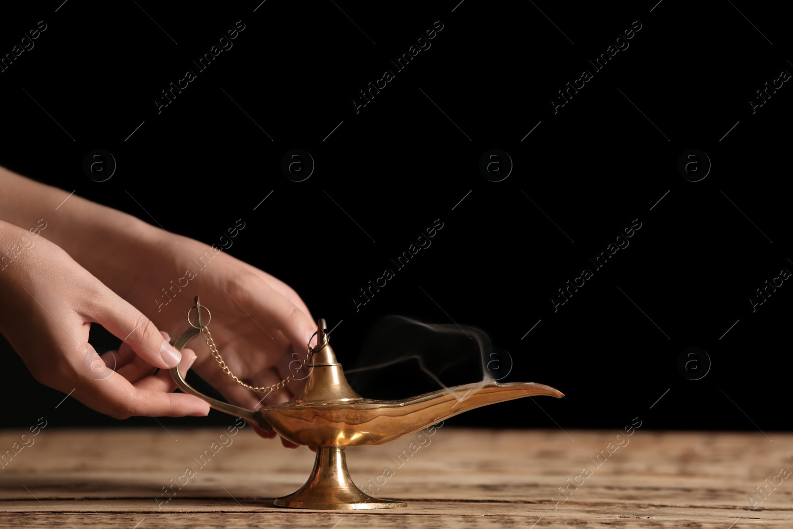 Photo of Woman rubbing magical Aladdin lamp on table against dark background