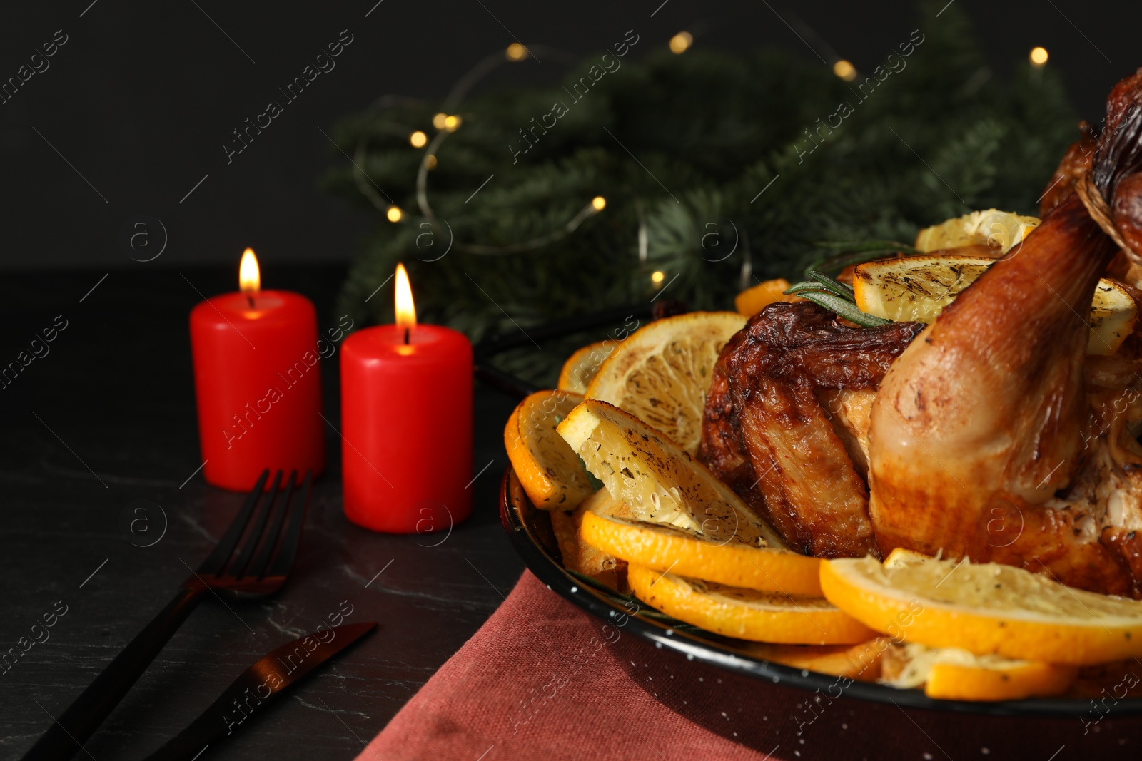 Photo of Baked chicken with orange slices and burning candles on black table, closeup