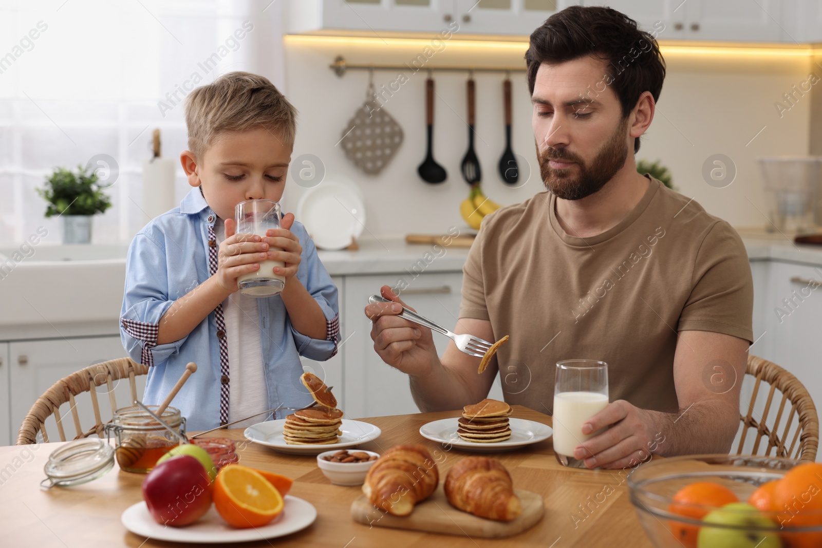 Photo of Father and his cute little son having breakfast at table in kitchen