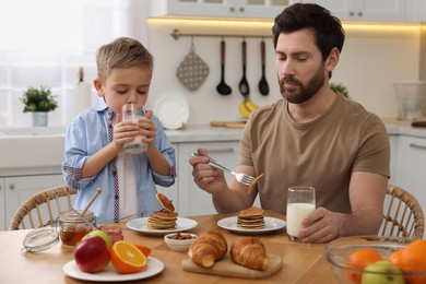 Photo of Father and his cute little son having breakfast at table in kitchen