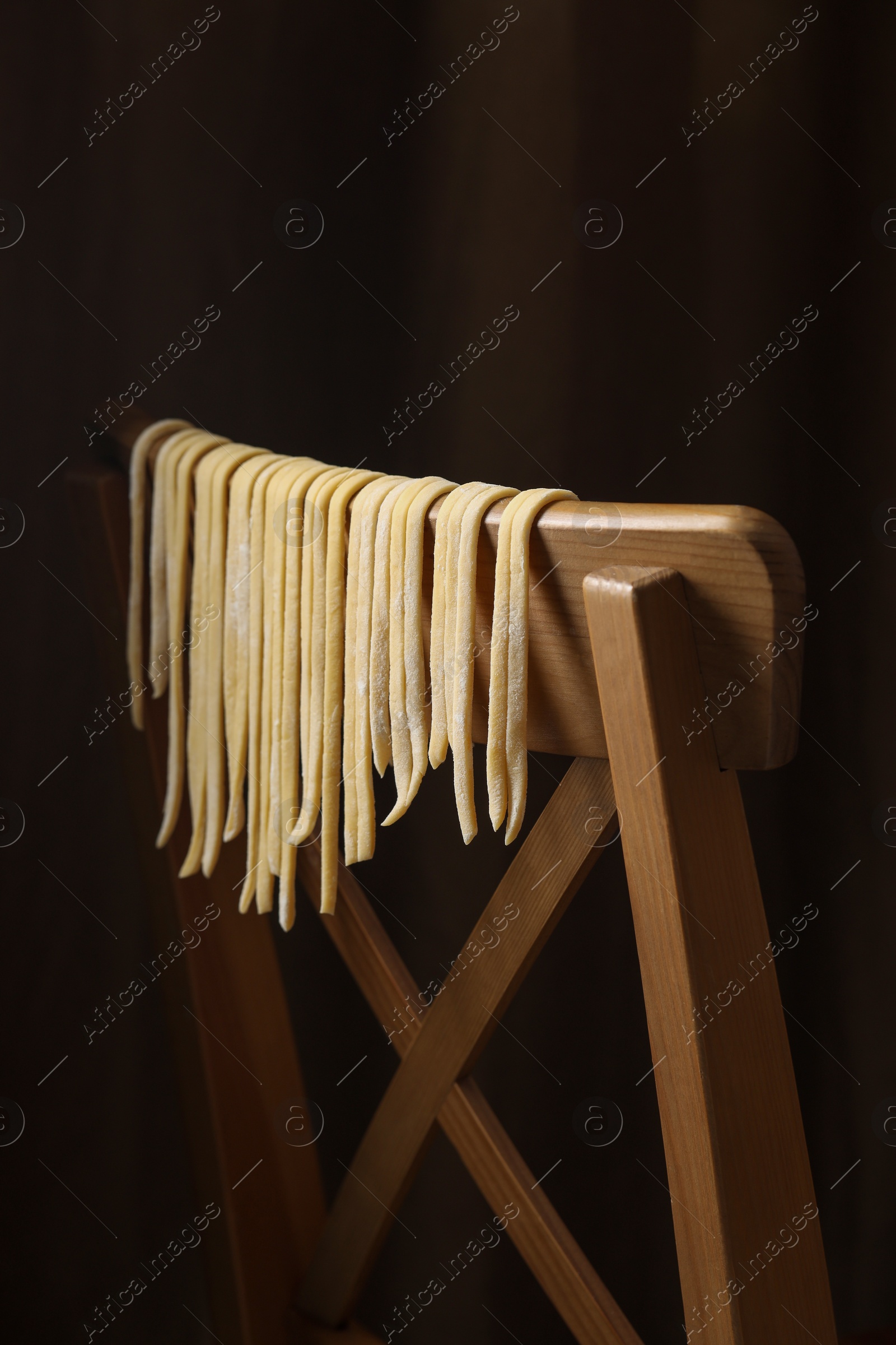 Photo of Homemade pasta drying on chair against dark background