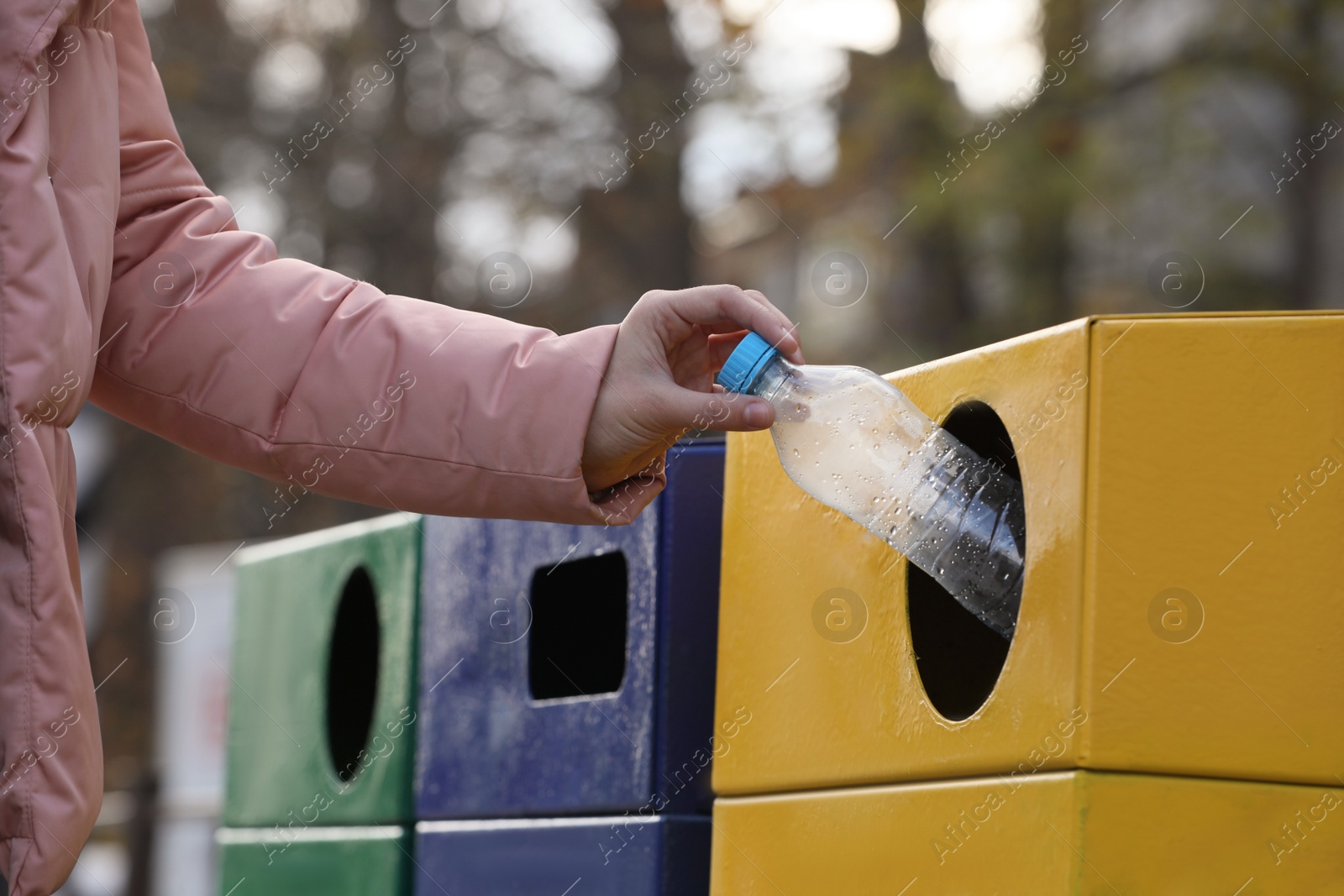 Photo of Woman throwing plastic bottle into garbage bin outdoors, closeup. Waste sorting