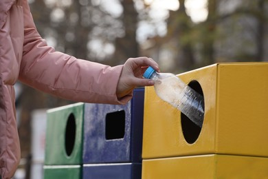 Woman throwing plastic bottle into garbage bin outdoors, closeup. Waste sorting