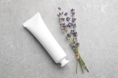 Tube of hand cream and lavender on light grey table, flat lay