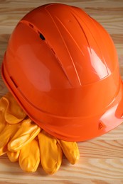 Hard hat and gloves on wooden table, closeup. Safety equipment