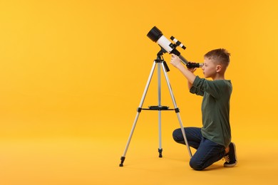 Little boy looking at stars through telescope on orange background, space for text