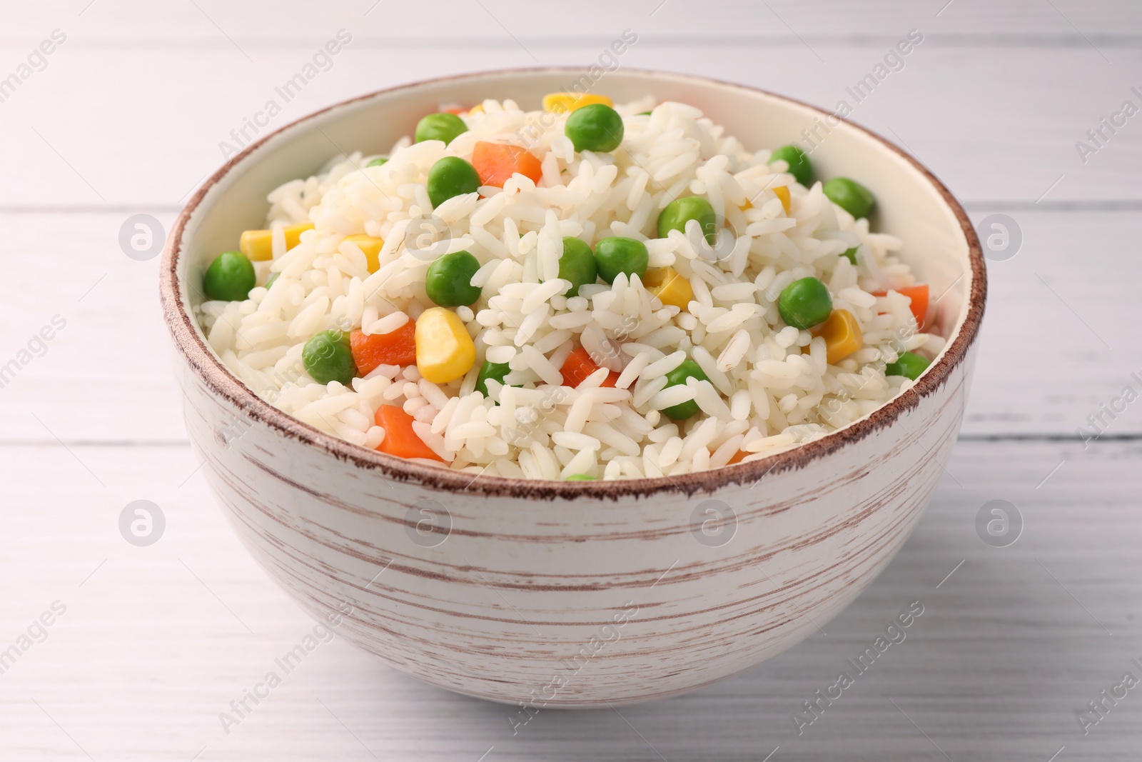 Photo of Bowl of delicious rice with vegetables on white wooden table, closeup