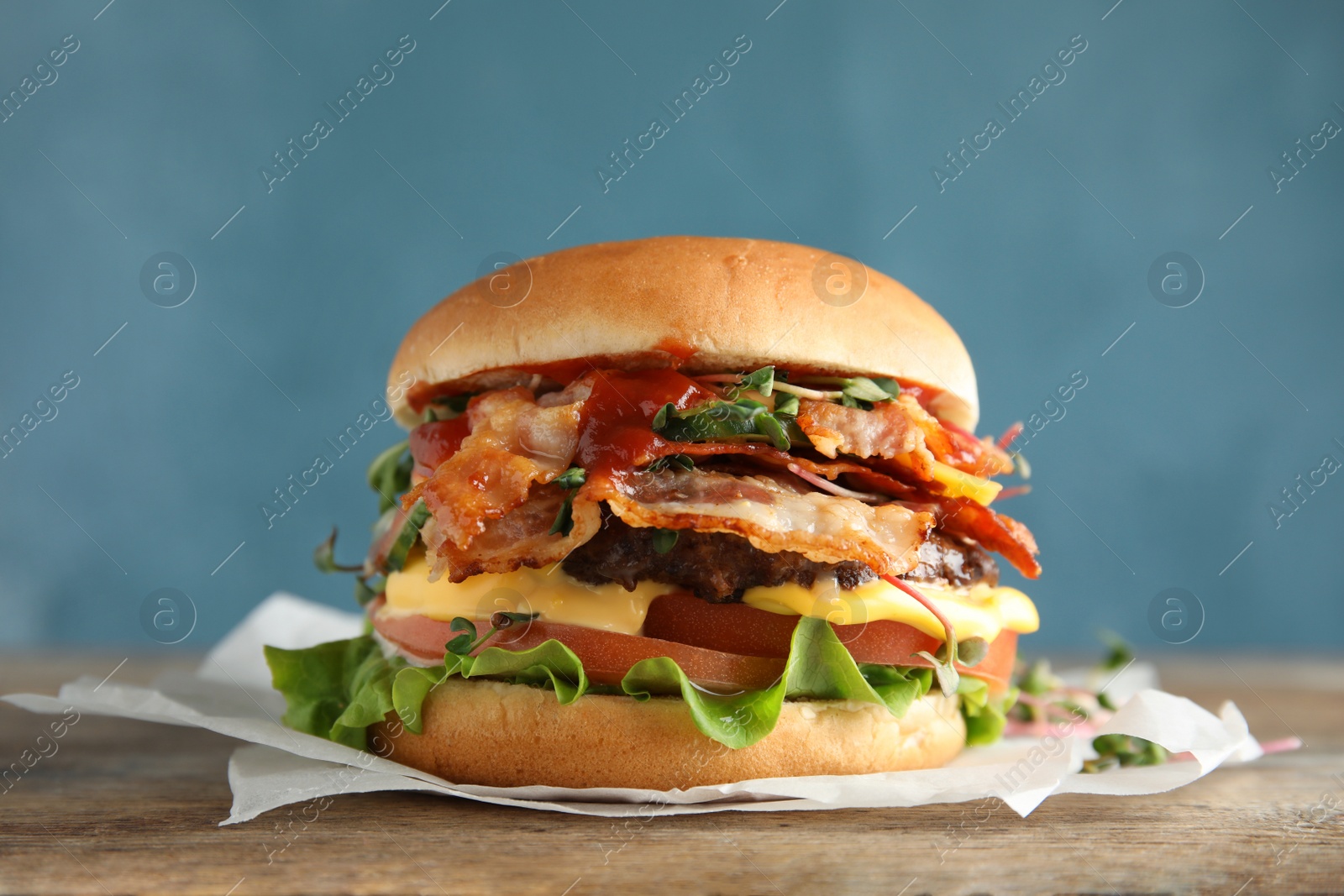 Photo of Tasty burger with bacon on table against color background