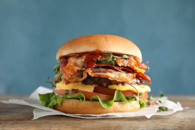 Tasty burger with bacon on table against color background
