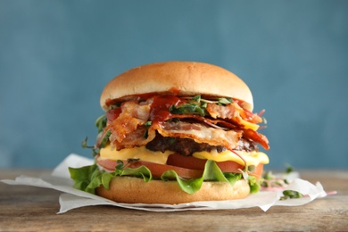 Photo of Tasty burger with bacon on table against color background