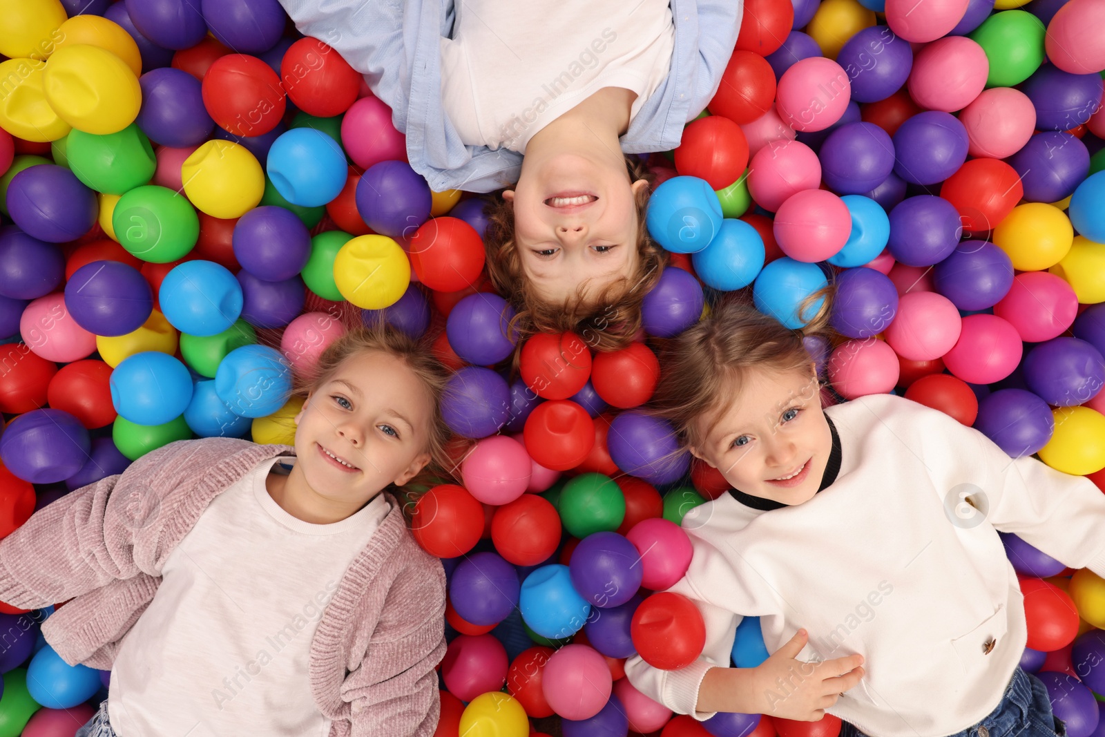 Photo of Happy little kids lying on many colorful balls, top view