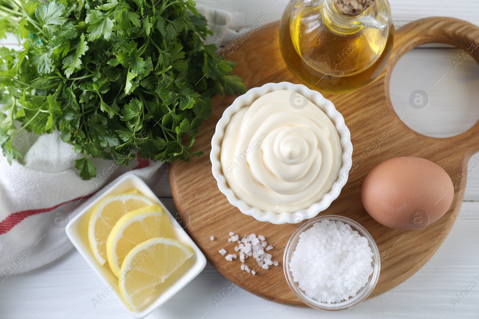 Photo of Fresh mayonnaise sauce in bowl and ingredients on white wooden table, flat lay