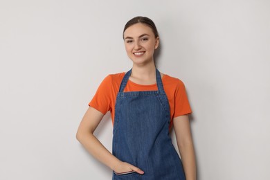 Beautiful young woman in clean denim apron on light grey background