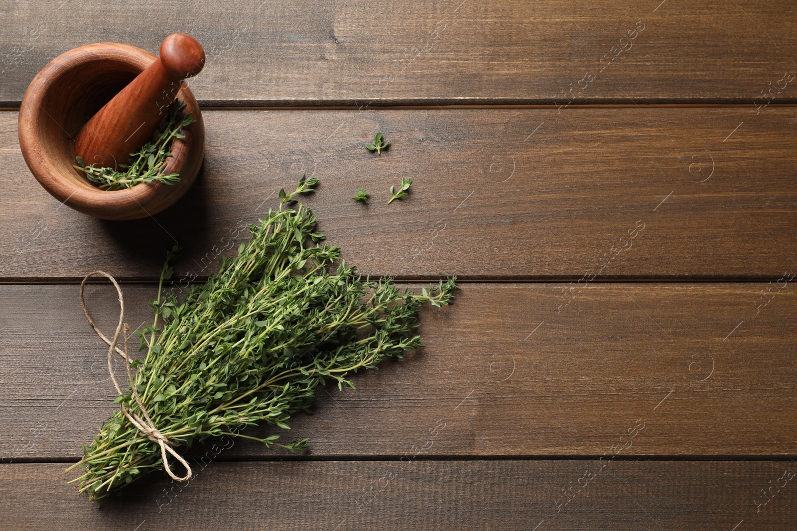 Photo of Bunch of aromatic thyme and mortar with pestle on wooden table, flat lay. Space for text