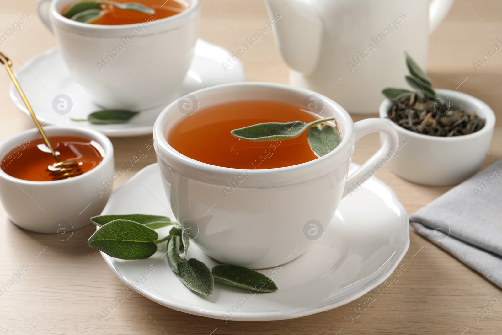 Photo of Cup of aromatic sage tea served with honey on wooden table