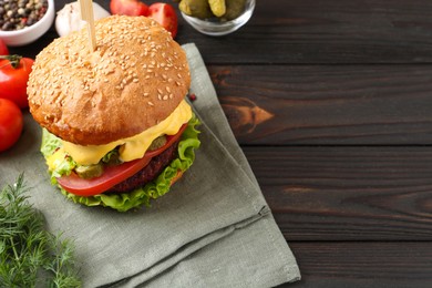 Photo of Delicious vegetarian burger and ingredients on wooden table, space for text