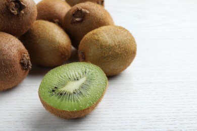 Photo of Cut and whole fresh kiwis on white wooden table, closeup. Space for text