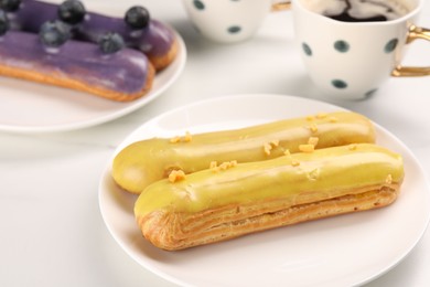 Tasty glazed eclairs on white table, closeup