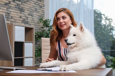 Photo of Beautiful woman with her dog sitting at table in home office