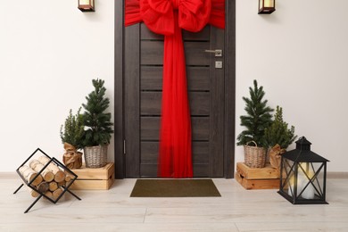 Photo of Wooden door with beautiful red bow near evergreen trees ,logs and lantern. Christmas decoration