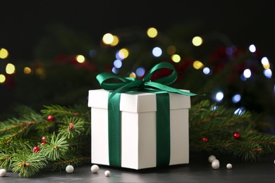 Photo of Christmas present. Beautiful gift box and fir tree branches on black table against blurred festive lights