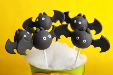 Photo of Delicious bat shaped cake pops on yellow background, closeup. Halloween treat
