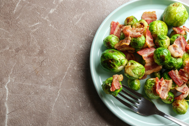 Photo of Delicious Brussels sprouts with bacon on marble table, above view. Space for text