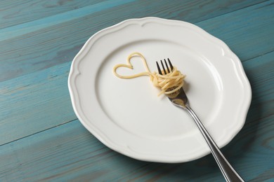 Photo of Heart made of tasty spaghetti and fork on light blue wooden table