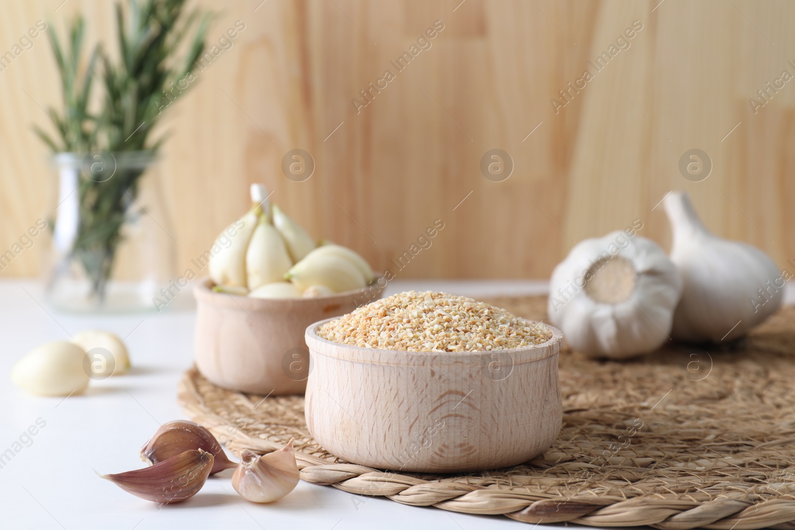 Photo of Dehydrated garlic granules in bowl, fresh bulbs and cloves on white table