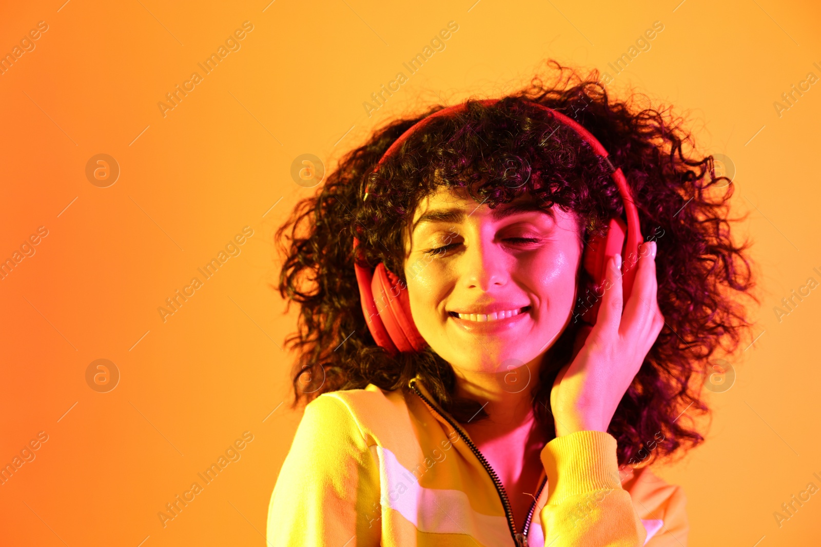 Photo of Beautiful young woman listening to music with headphones on color background in neon lights