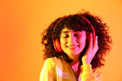 Photo of Beautiful young woman listening to music with headphones on color background in neon lights