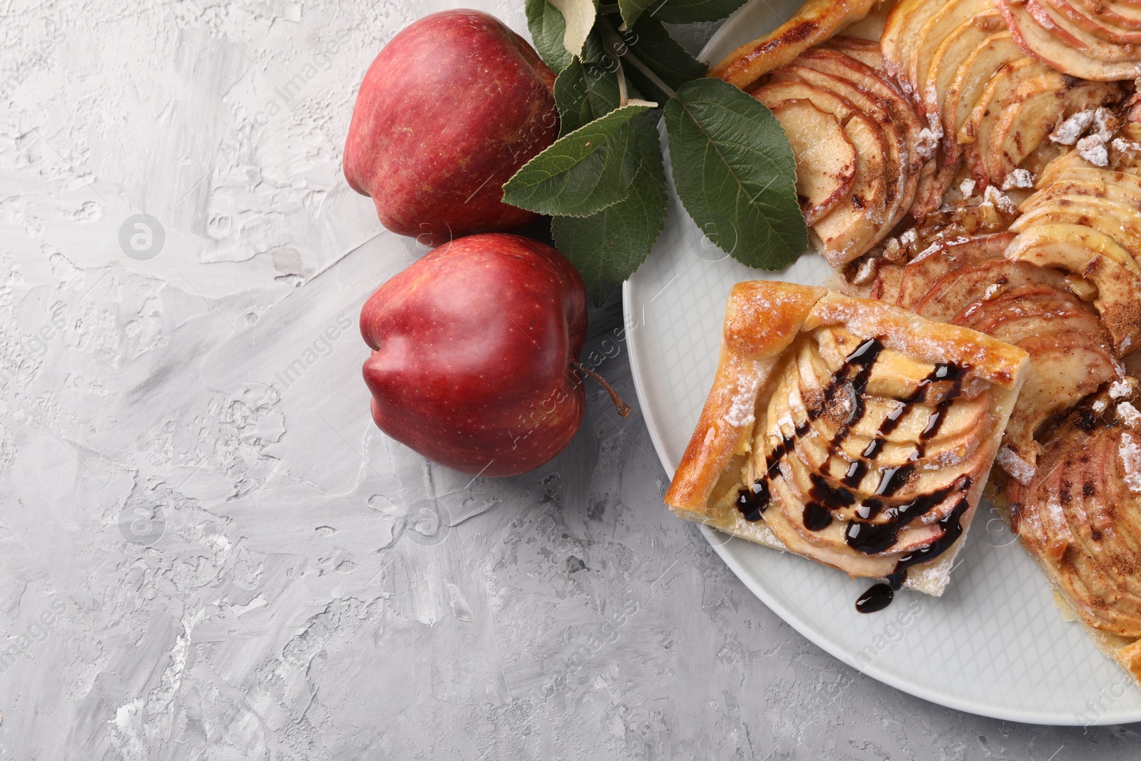 Photo of Tasty apple pie with chocolate topping, fresh fruits and green leaves on light grey textured table, flat lay. Space for text