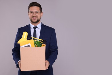Happy unemployed man with box of personal office belongings on grey background. Space for text