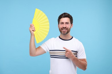 Photo of Happy man holding hand fan on light blue background