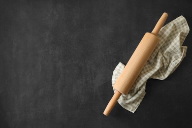 Rolling pin and kitchen towel on black table, top view. Space for text