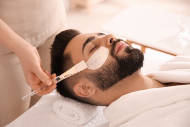 Cosmetologist applying mask on man's face in spa salon