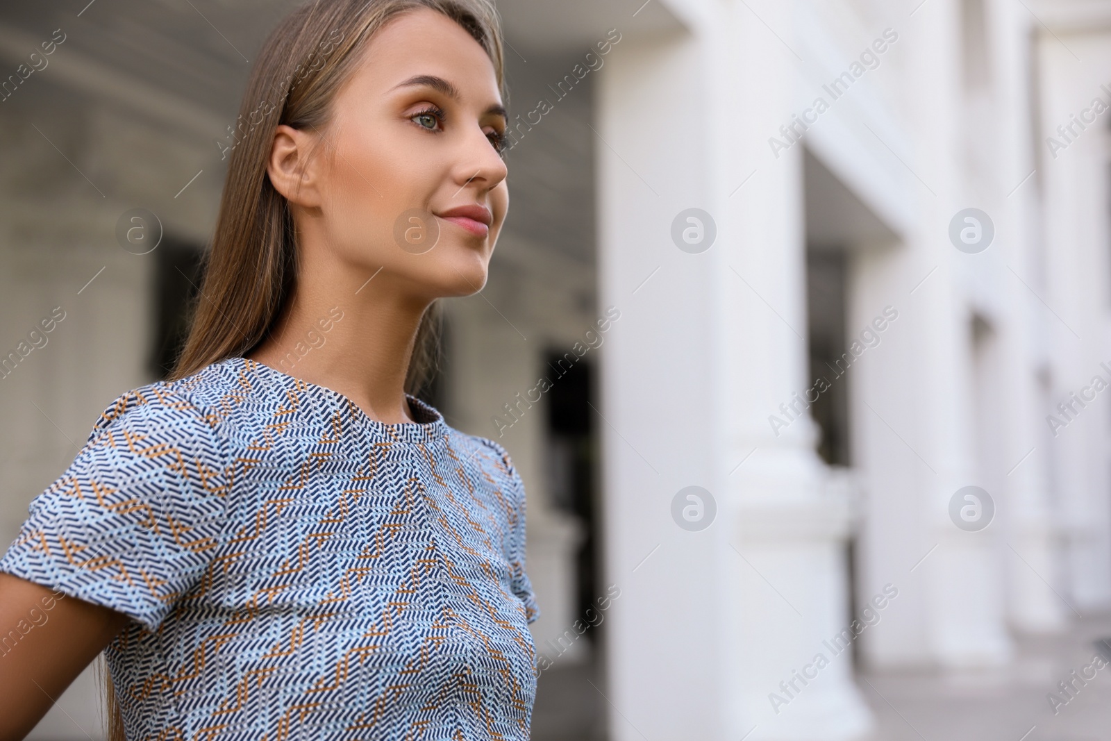 Photo of Beautiful young woman in stylish t-shirt near building outdoors, space for text