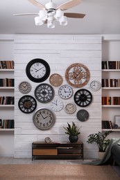 Photo of Stylish room interior with console table, beautiful houseplants and collection of different clocks on white wall