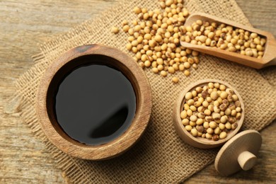 Photo of Soy sauce in bowl and soybeans on wooden table, flat lay