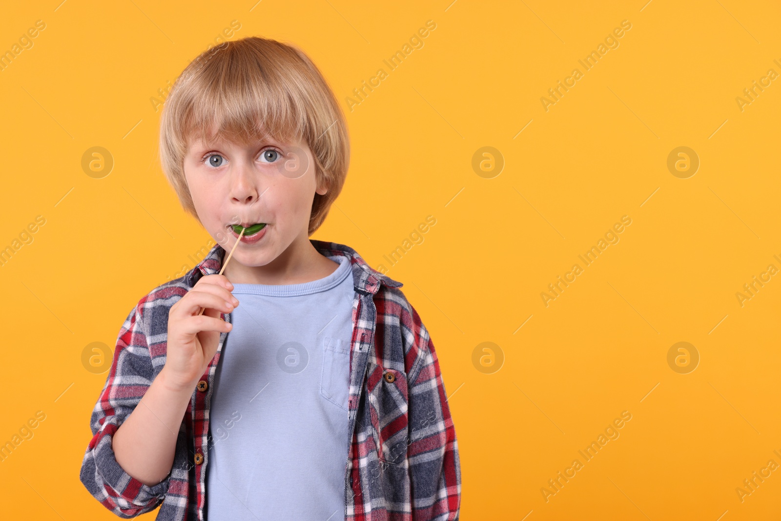 Photo of Cute little boy licking lollipop on orange background, space for text