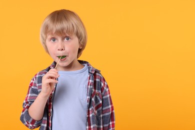 Photo of Cute little boy licking lollipop on orange background, space for text