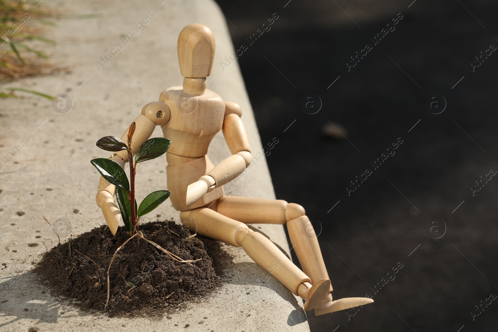 Photo of Wooden human figure with soil and green seedling outdoors, space for text