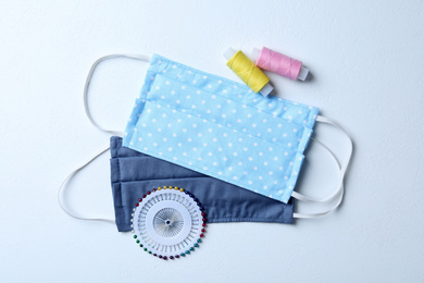 Homemade protective masks, threads and sewing pins on white background, flat lay