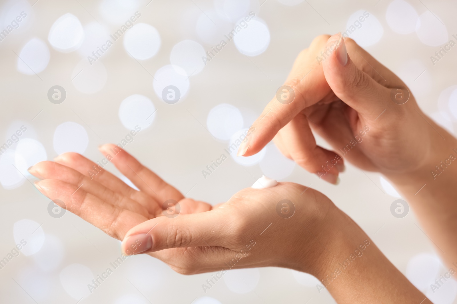 Photo of Woman applying hand cream on blurred background, closeup