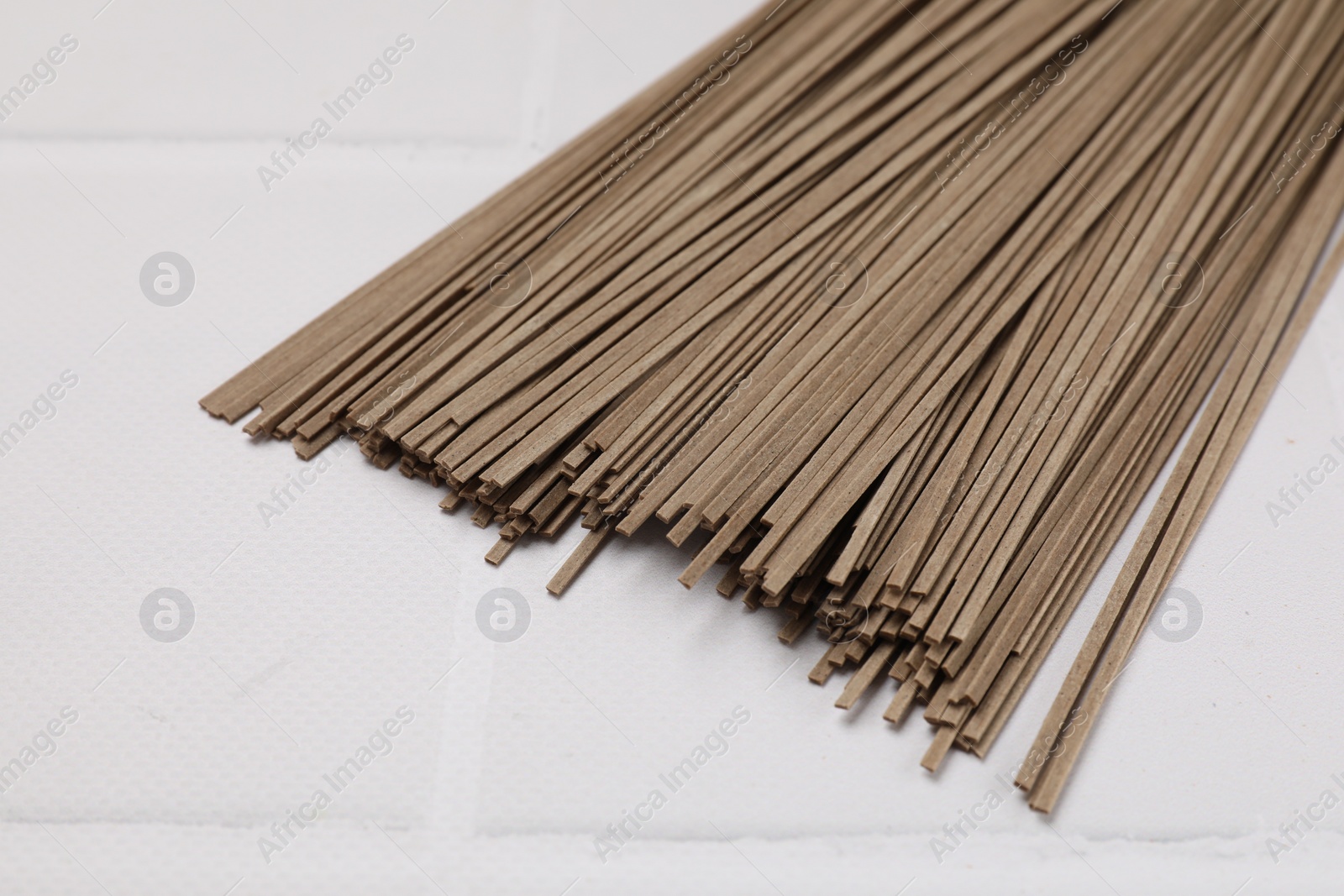 Photo of Uncooked buckwheat noodles (soba) on white tiled table, closeup