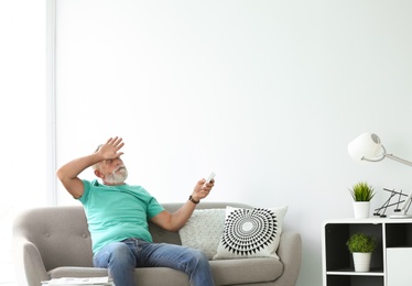 Photo of Senior man with air conditioner remote control suffering from heat at home