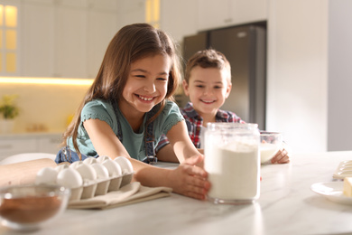 Cute little children cooking dough in kitchen at home