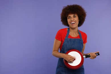 Photo of Happy young woman with frying pan having fun on purple background. Space for text