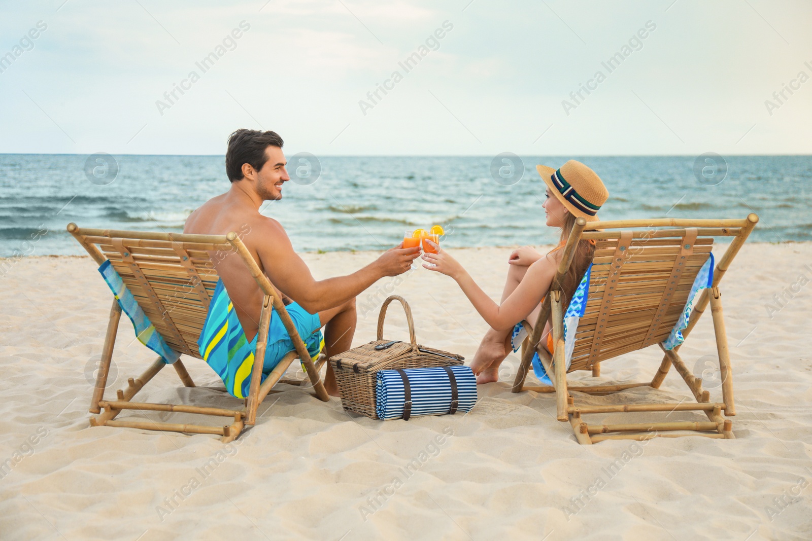 Photo of Happy young couple with cocktails sitting on deck chairs at sea beach